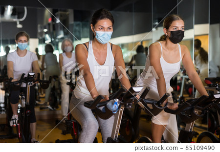 Women in masks training on stationary bikes Women in masks training on stationary bikes 85109490