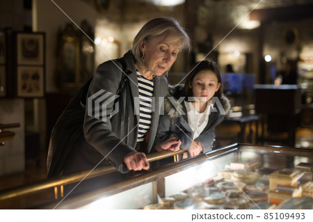 Aged female tutor with preteen girl exploring showpieces in museum Aged female tutor with preteen girl exploring showpieces in museum 85109493