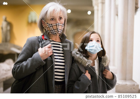 Preteen girl in protective mask visiting museum of ancient sculptures with grandmother Preteen girl in protective mask visiting museum of ancient sculptures with grandmother 85109525