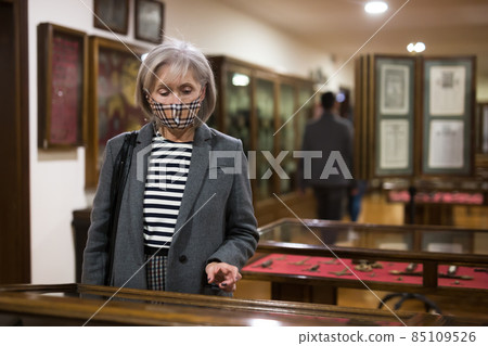 Focused elderly woman in mask observing arts and crafts in gallery Focused elderly woman in mask observing arts and crafts in gallery 85109526