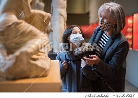 Preteen girl in protective mask visiting museum of ancient sculptures with grandmother Preteen girl in protective mask visiting museum of ancient sculptures with grandmother 85109527