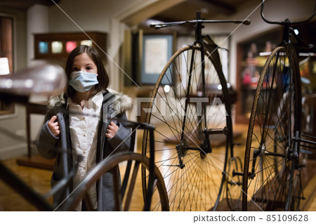 Preteen girl in protective mask viewing vintage bicycles in museum Preteen girl in protective mask viewing vintage bicycles in museum 85109628