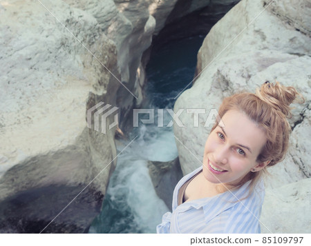 Smiling girl looks up from the bottom while standing on the edge of the canyon over the river 85109797