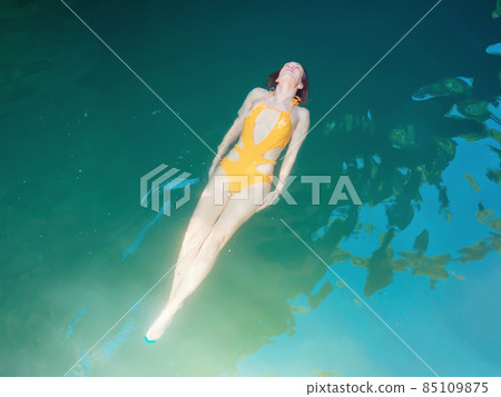 A girl in a yellow swimsuit stretched out swims on her back in a clean turquoise pond A girl in a yellow swimsuit stretched out swims on her back in a clean turquoise pond 85109875