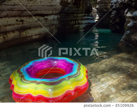 Swimming ring with a multicolored pattern on clear turquoise water in a shady canyon gorge 85109926