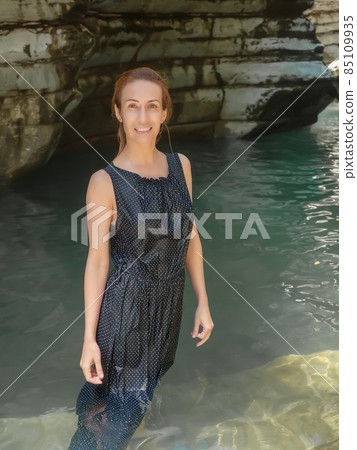 Smiling girl in a wet dress stands by a pond in a shady lagoon among canyons 85109935
