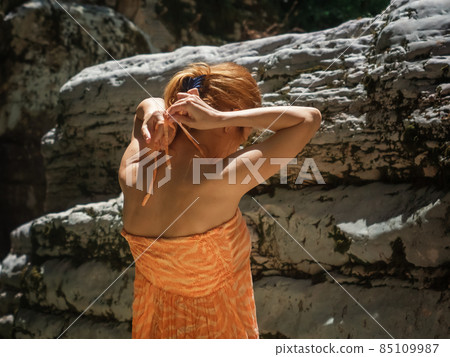 Girl ties the straps of a sundress while standing outdoors in the canon area 85109987