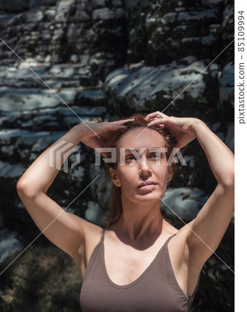 Portrait of a girl holding her hands on her head in the sun, surrounded by rocks. Art photography 85109994