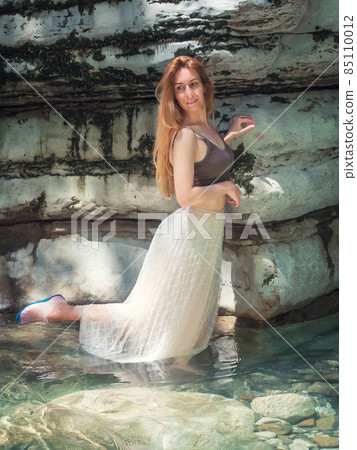 A girl stands in clear water near a mossy canyon with her leg back above the water 85110012
