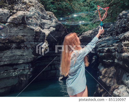 Redhaired girl blows big soap bubbles in the canyon gorge by the water 85110097