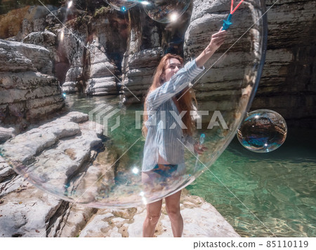 The girl blows huge soap bubbles into the canyon gorge near the clear river. View through the bubble The girl blows huge soap bubbles into the canyon gorge near the clear river. View through the bubble 85110119
