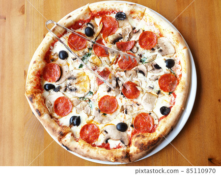 Fresh pizza with mushrooms, sausage and olives stands on a wooden table. Top view 85110970