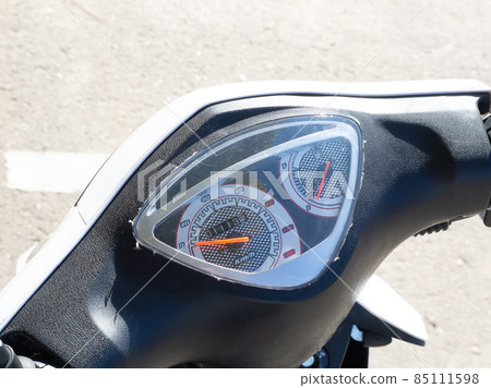 A fragment of a motorcycle steering wheel with a speedometer outdoor. Closeup photo A fragment of a motorcycle steering wheel with a speedometer outdoor. Closeup photo 85111598