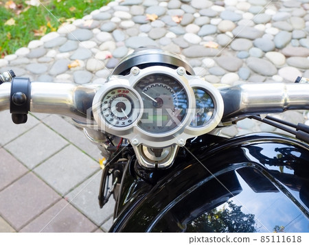 Motorcycle handlebar with circular speedometer against the background of paving slabs and decorative masonry Motorcycle handlebar with circular speedometer against the background of paving slabs and decorative masonry 85111618