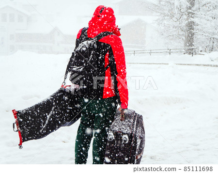 Man with luggage stands on the road of a ski resort during heavy snowfall Man with luggage stands on the road of a ski resort during heavy snowfall 85111698