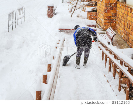 A worker clears snow from a descent from a house during a heavy snowfall 85112163