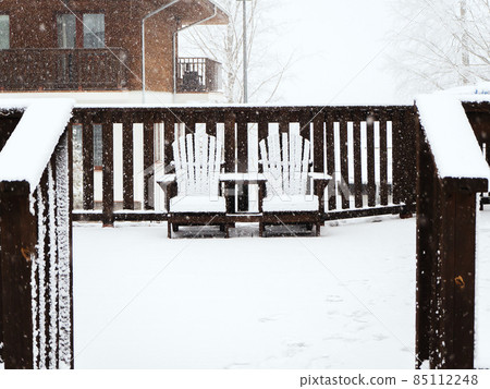 Two wooden garden chairs stand together on a terrace covered with snow in winter during snowfall Two wooden garden chairs stand together on a terrace covered with snow in winter during snowfall 85112248