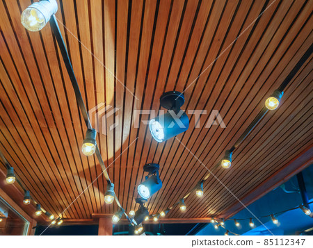 Spotlights and bulbs hang on a metal frame under a wooden canopy Spotlights and bulbs hang on a metal frame under a wooden canopy 85112347