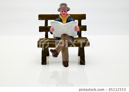 A man reading a newspaper on the bench 85112553