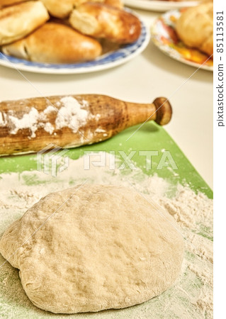 Raw dough and rolling pin near homemade pies in kitchen 85113581