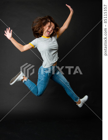 Happy cool ecstatic energetic girl jumping up midair dark background, jump 85115357