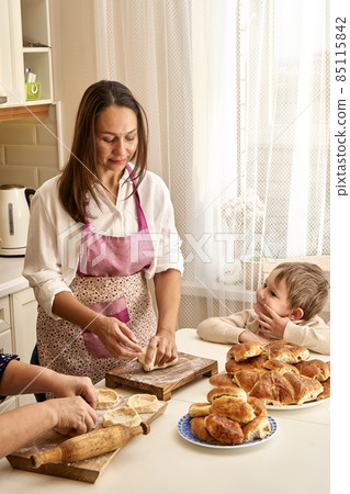 Woman kneads dough with mother and little son in kitchen 85115842