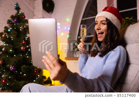 Emotional young girl using tablet, talking with friends by means of video calling. Christmas home decorations. 85117400