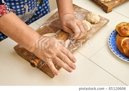 Senior lady rolls raw dough piece for pies in light kitchen 85120606