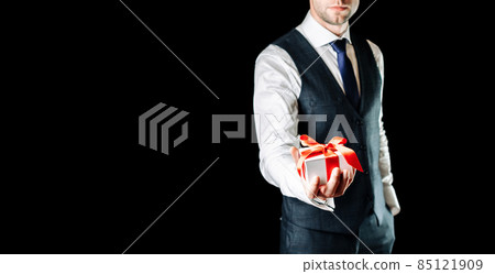 Gift man. Happy young businessman holding surprise gift box present with red ribbon isolated on black background. Black Friday, Valentine Day congratulations banner. Gift man. Happy young businessman holding surprise gift box present with red ribbon isolated on black background. Black Friday, Valentine Day congratulations banner. 85121909