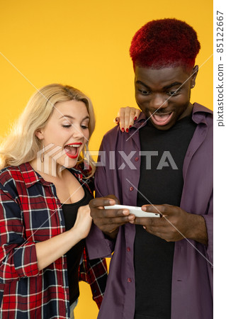 Phone gaming. Gadget leisure. Smartphone nerd. Mobile entertainment. Happy excited millennial friends man woman playing game app isolated on yellow background. Phone gaming. Gadget leisure. Smartphone nerd. Mobile entertainment. Happy excited millennial friends man woman playing game app isolated on yellow background. 85122667