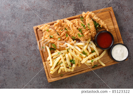Crispy deep fried chicken strips with sauces and french fries closeup on the wooden tray. Horizontal top view 85123322