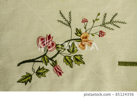 Garland of embroidered branches of red and yellow roses with buds intertwined with a coniferous branch and red berries on a white cotton fabric. Garland of embroidered branches of red and yellow roses with buds intertwined with a coniferous branch and red berries on a white cotton fabric. 85124356