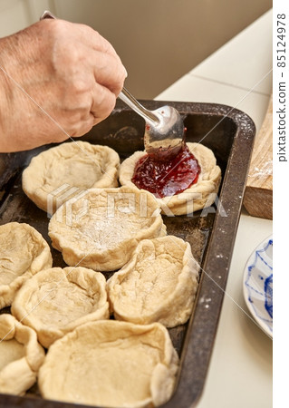 Senior woman fills raw pies with natural jam in kitchen Senior woman fills raw pies with natural jam in kitchen 85124978