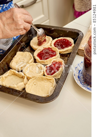 Senior woman fills raw pies with natural jam in kitchen Senior woman fills raw pies with natural jam in kitchen 85124981
