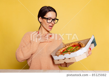 Young surprised girl holding box with pizza isolated on yellow studio background. World pizza day Young surprised girl holding box with pizza isolated on yellow studio background. World pizza day 85125082