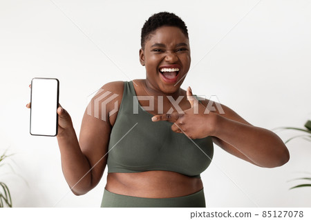 Joyful sporty african american plus size woman showing cellphone, mockup 85127078