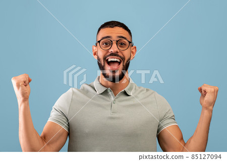 Satisfied happy arab man rejoicing to success and shouting in excitement, standing on blue background 85127094