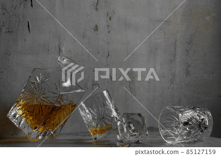 Glass of the whiskey with a square decanter on a grey clay textured  background. 85127159
