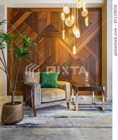 Modern beige armchair, small coffee table, planter, and modern tall glass chandelier, and decorated wood cladding wall 85128656