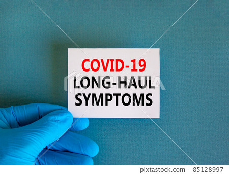 COVID-19 long-haul covid symptoms symbol. White card with words Covid-19 long-haul symptoms. Doctor hand, blue background, copy space. Medical, COVID-19 long-haul covid symptoms concept. 85128997