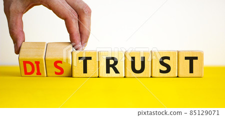 Distrust or trust symbol. Businessman turns wooden cubes, changes words 'distrust' to 'trust'. Beautiful yellow table, white background. Business and distrust or trust concept, copy space. 85129071
