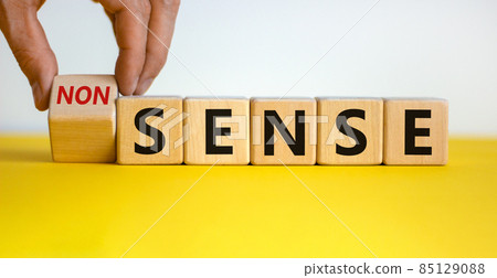 Hand flips a cube and changes the word 'nonsense' to 'sense' or vice versa. Beautiful yellow table, white background. Concept. Copy space. 85129088
