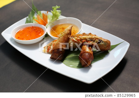Fried spring rolls on a white plate and spicy sauce 85129965