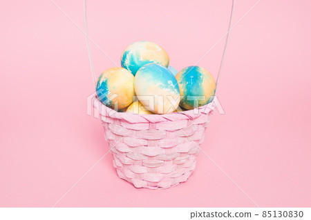 Multi-colored Easter eggs in a basket on a pink isolated background. Easter is a bright holiday. Multi-colored Easter eggs in a basket on a pink isolated background. Easter is a bright holiday. 85130830