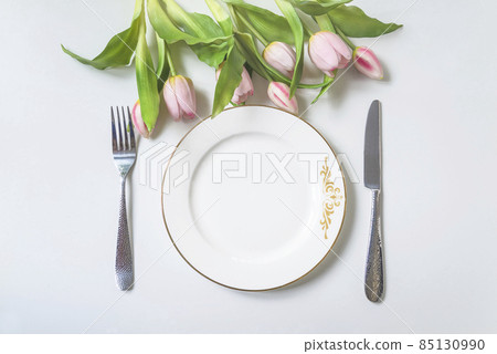 Spring holiday place setting; Top view of white plate, fork and knife and bouquet of pink tulips above 85130990