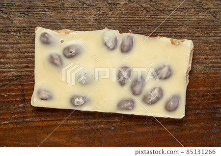 piece of white chocolate with almonds on wood piece of white chocolate with almonds on wood 85131266
