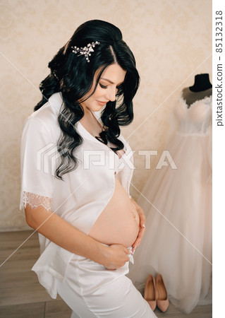 beautiful pregnant bride brunette in white pajamas with bare tummy. beautiful pregnant bride brunette in white pajamas with bare tummy. 85132318