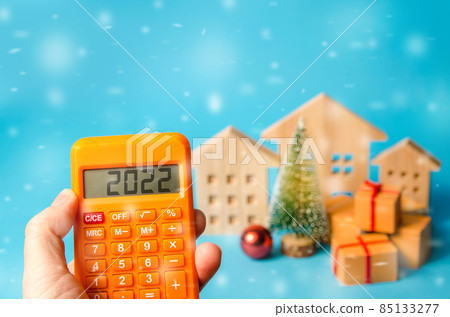 Calculator 2022, Christmas tree and miniature houses. Accumulating money and planning a budget. Business and finance. Loans, deposit, credit. Promotions, offers. Selective focus Calculator 2022, Christmas tree and miniature houses. Accumulating money and planning a budget. Business and finance. Loans, deposit, credit. Promotions, offers. Selective focus 85133277