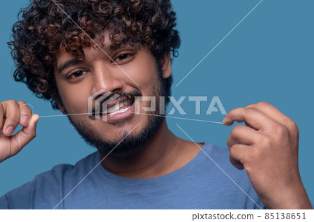 Smiling guy with curly hair flossing his teeth Smiling guy with curly hair flossing his teeth 85138651