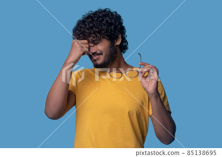 Tired curly-haired bearded guy suffering from eyestrain Tired curly-haired bearded guy suffering from eyestrain 85138695